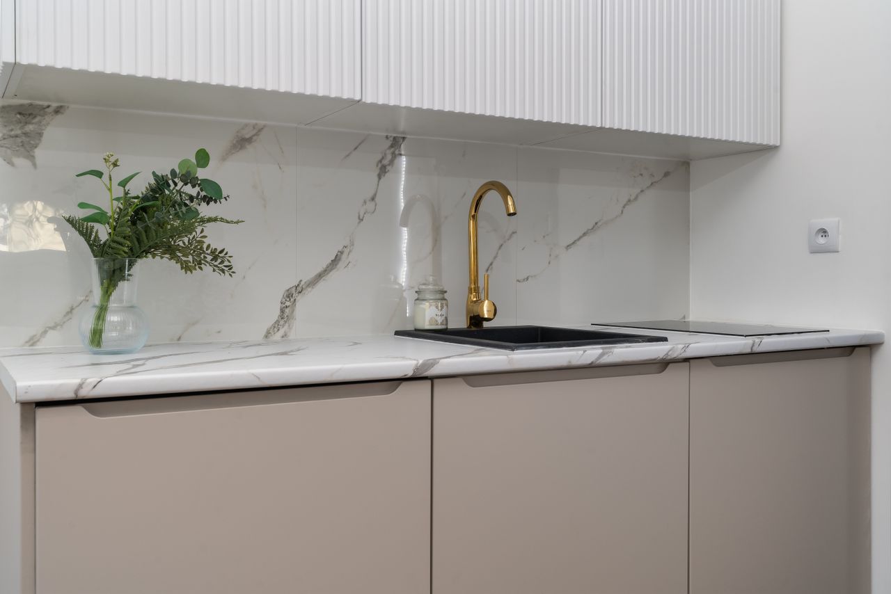 About Elegant kitchen interior with marble counters and a gold faucet, featuring greenery for a touch of nature.